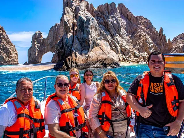 Un groupe de personnes portant des gilets de sauvetage pose pour une photo sur un bateau près de formations rocheuses.