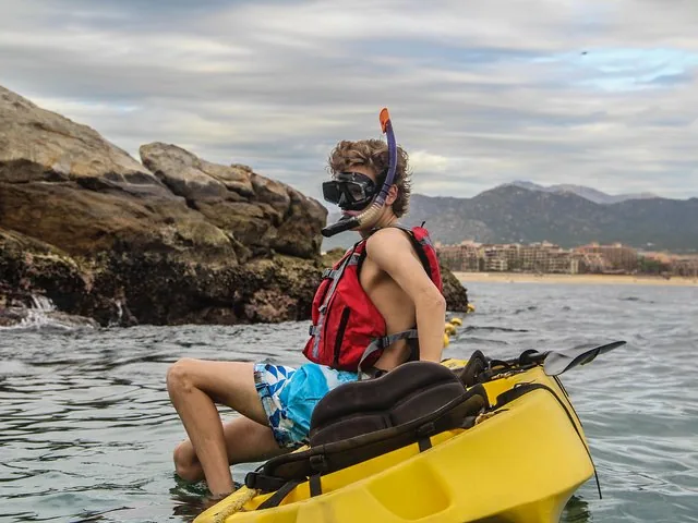 Un jeune homme équipé de matériel de snorkeling et d'un gilet de sauvetage est assis sur un kayak jaune.