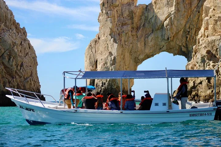 Un petit bateau blanc transporte des passagers près d'une grande arche naturelle en pierre dans l'océan.