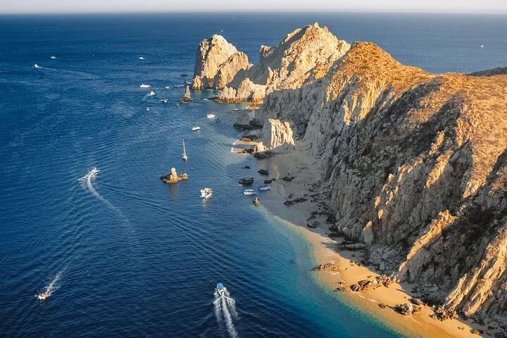 Aerial view of boats near rocky cliffs and a beach along the coastline.